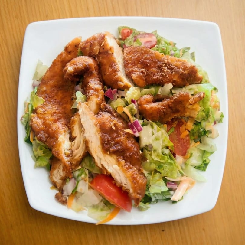 Crispy fried chicken pieces on a bed of fresh green salad with tomatoes and red onion.