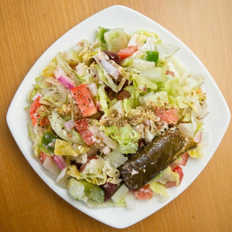 A fresh salad with lettuce, tomatoes, onions, and a stuffed grape leaf on a white plate.