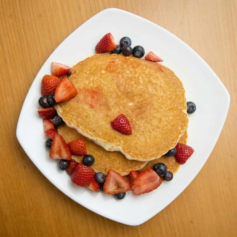 Golden pancakes topped with fresh strawberries and blueberries on a white plate.