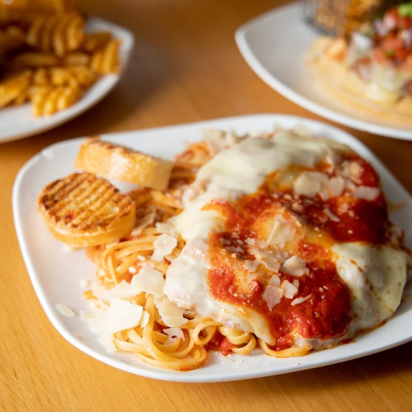 Gramercy Kitchen's linguine pasta with red sauce, melted cheese, and grilled bread on a white plate.