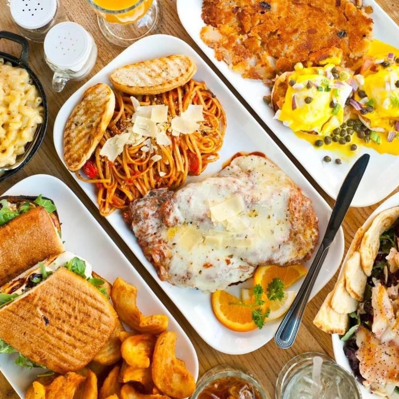 Overhead view of a diner spread including mac and cheese, pasta, chicken parmesan, eggs benedict, and sandwiches.