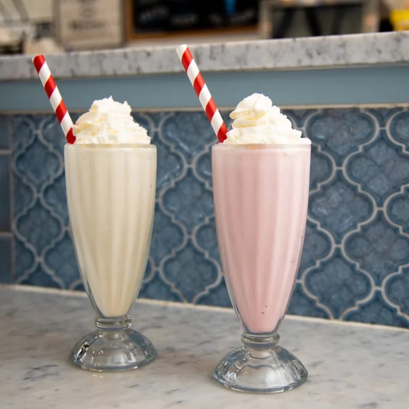 Two diner milkshakes, one vanilla and one strawberry, topped with whipped cream and striped straws.